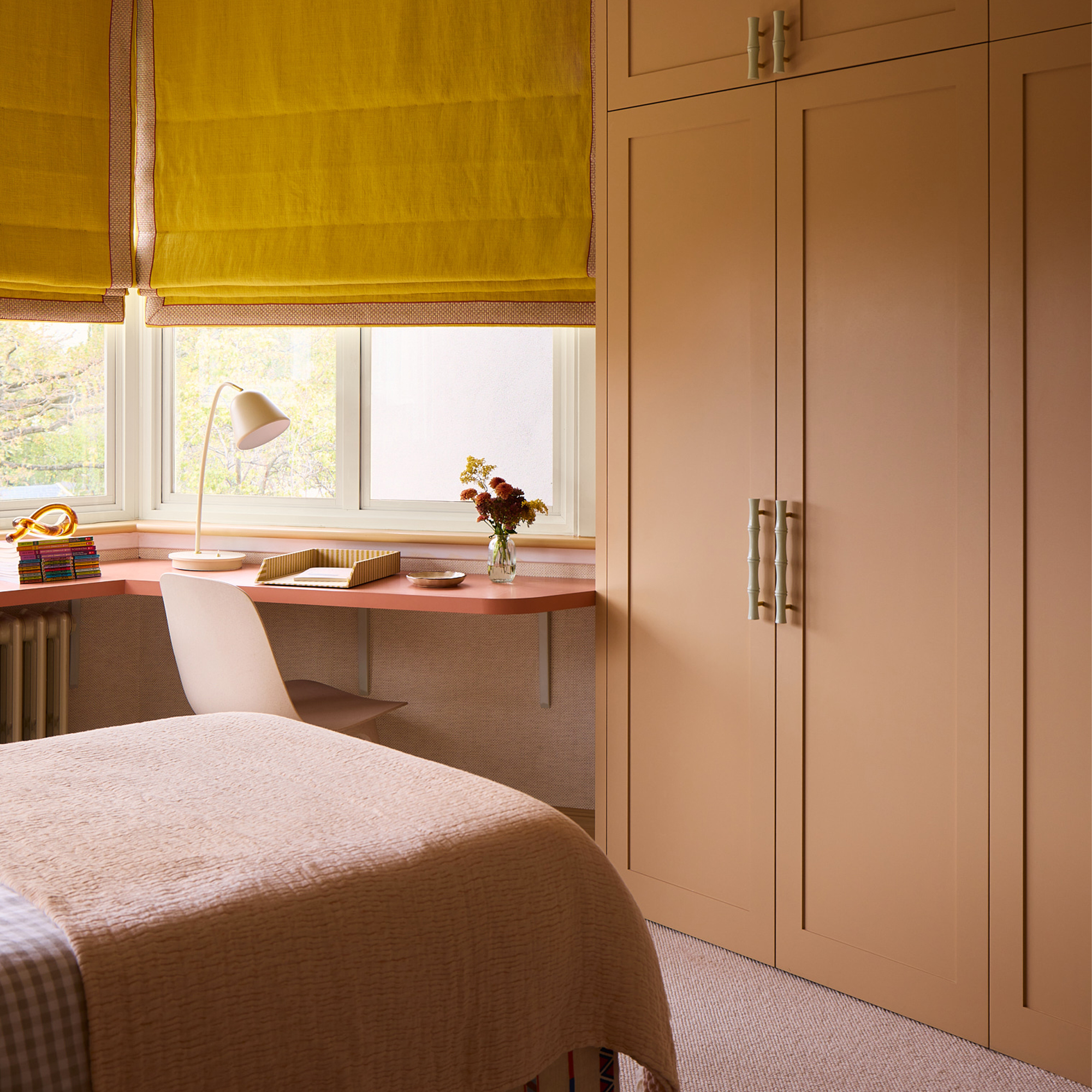 A bedroom with peach coloured wardrobes and a peach slimline desk in the window