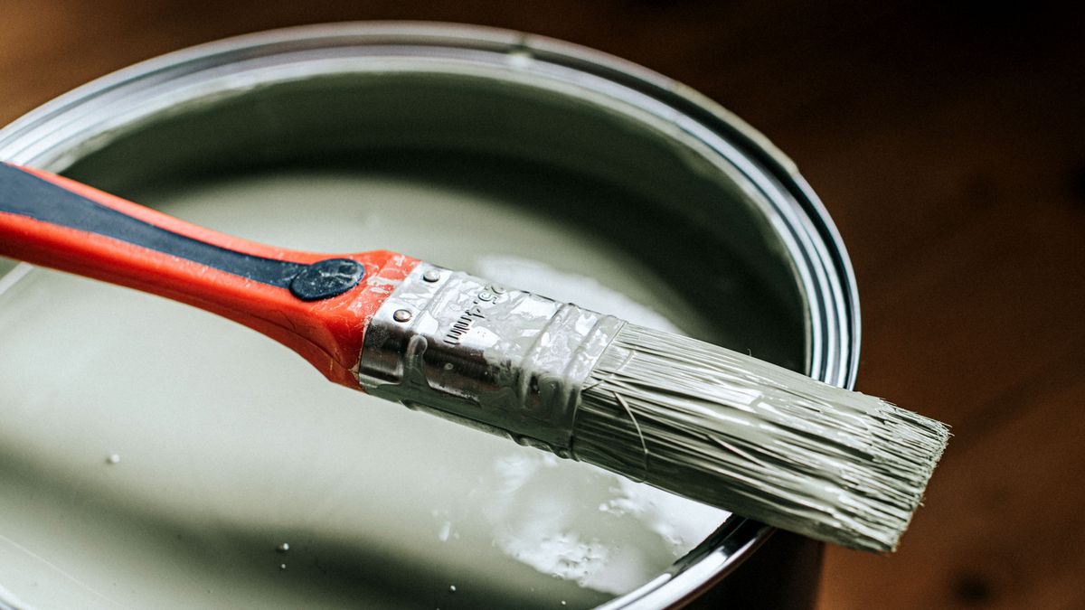 Paintbrush resting on top of open tin of green paint