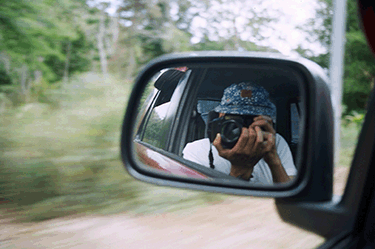 Reflection of Alex Mayo with camera in a car's side mirror