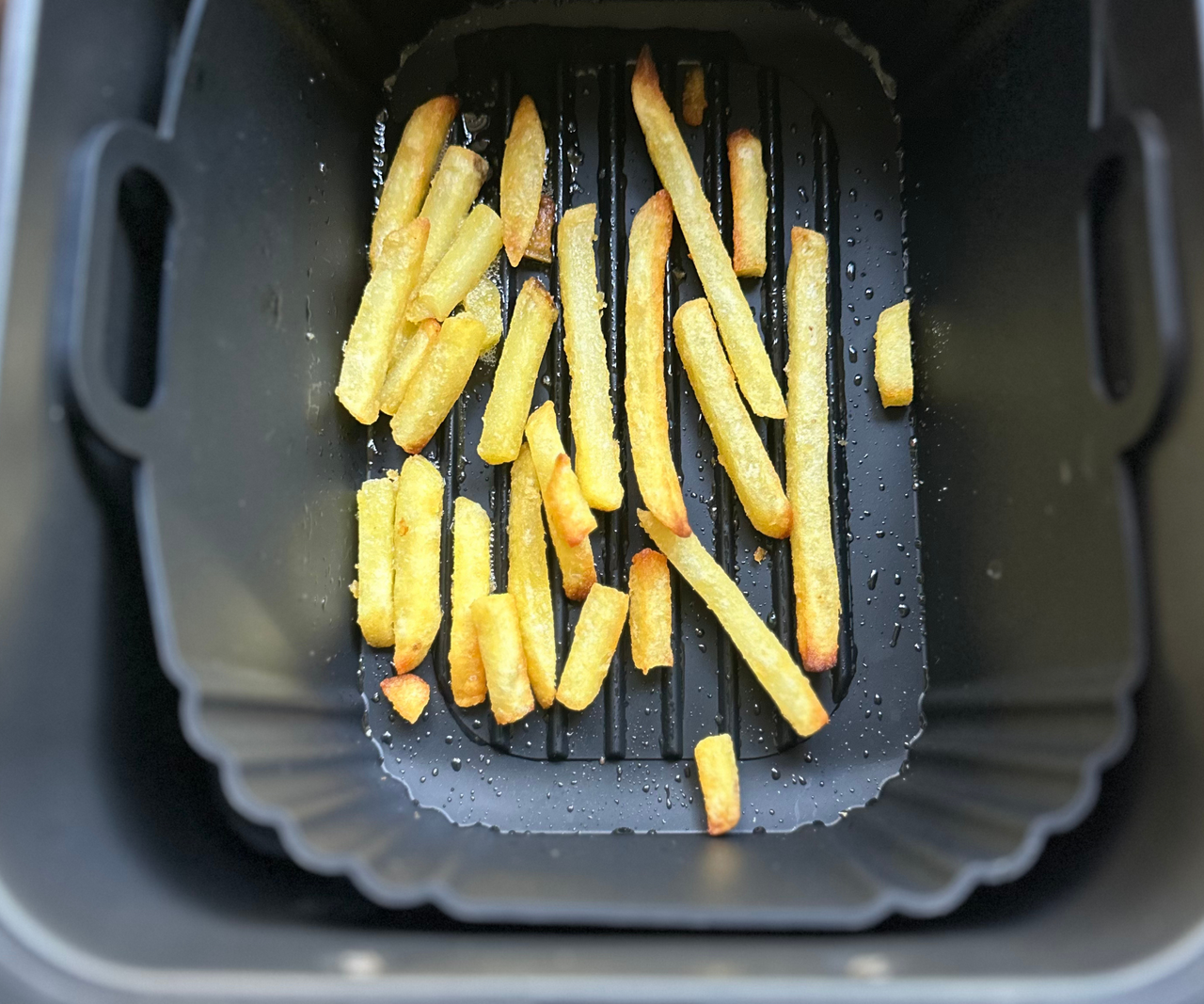 A black silicone air fryer basket with a few fries in the base, inside a black air fryer drawer.