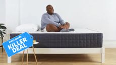 A man sits cross-legged on top of a Helix Plus mattress, in a white bedroom