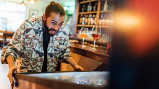 Cheerful bearded man playing pinball in bar - stock photo