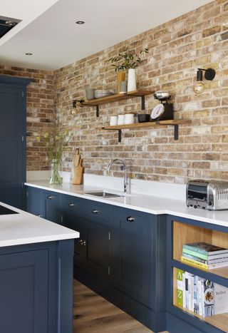 blue kitchen with white countertops, exposed brick wall and shelving