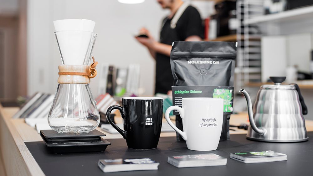 The Moleskine branding and logo extends onto cups and coffee bean bags