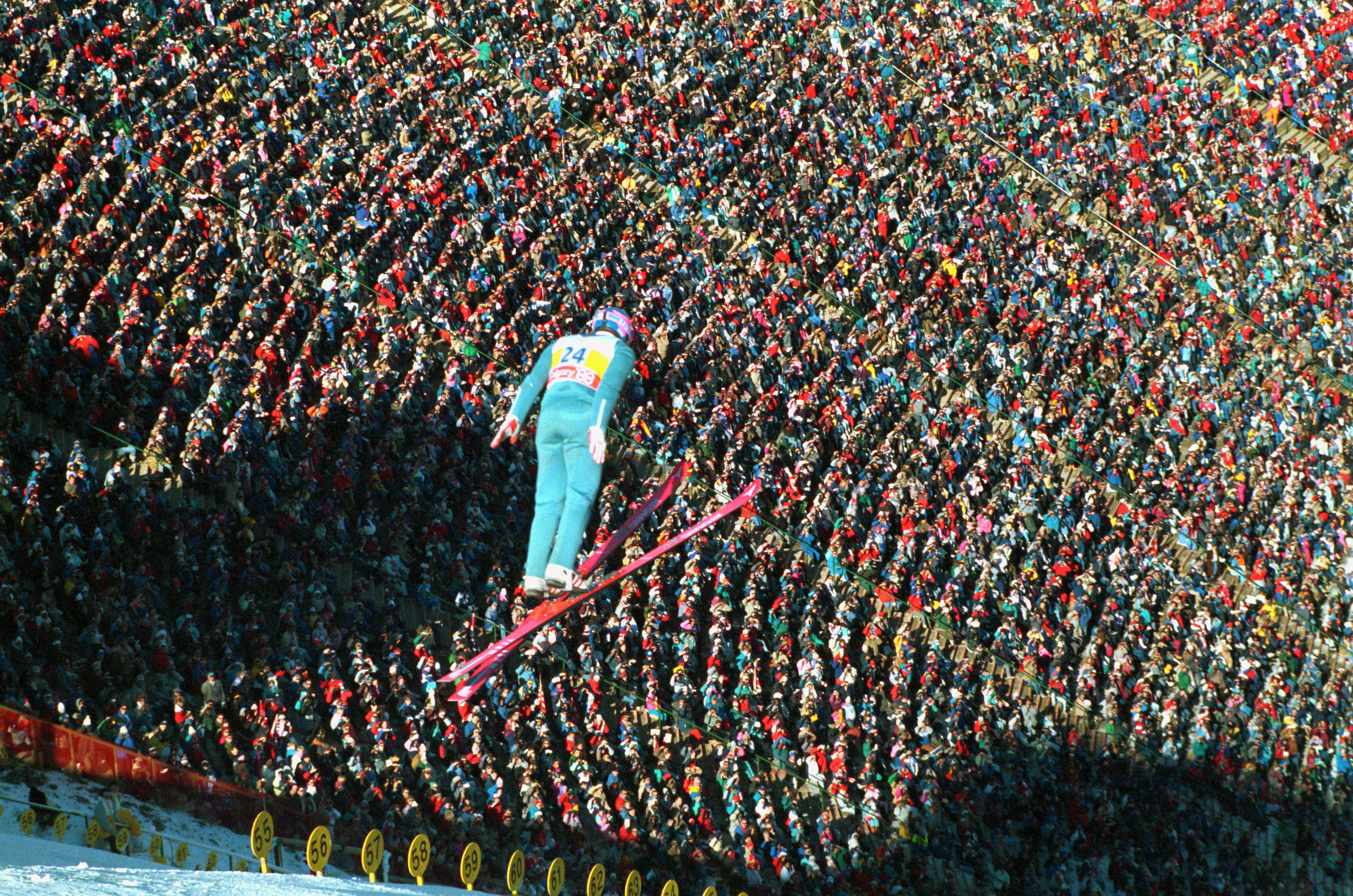 Eddie The Eagle Edwards soars over the crowd as he makes his second jump of the day during the 90 meter ski jump competition today. Edwards, Britain's lone ski jumper, finished last.