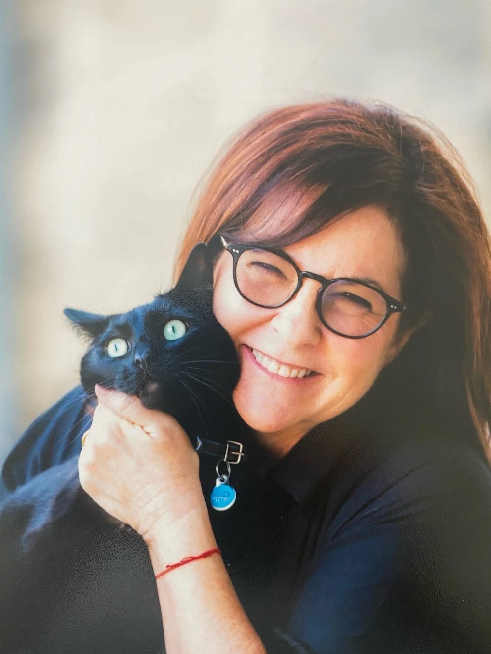 A headshot of a woman with dark hair and glasses holding a black cat and smiling