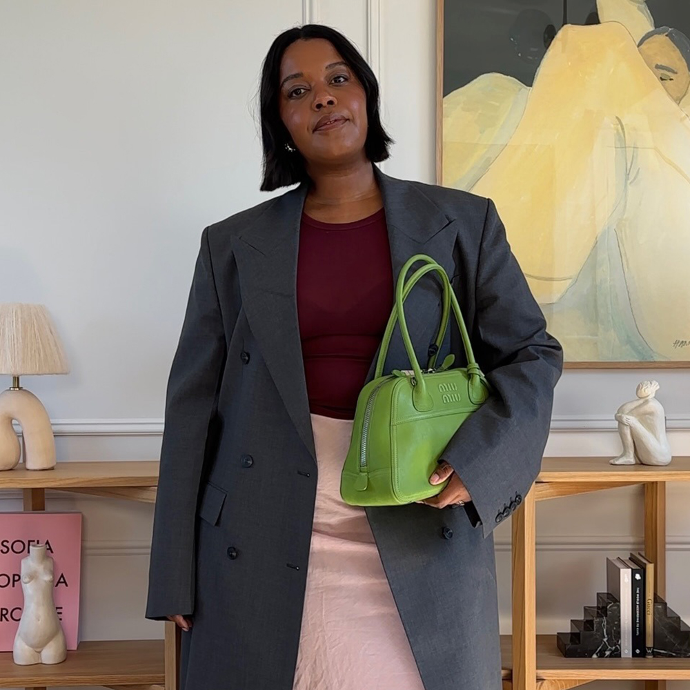 Woman wears grey coat, burgundy top, pink skirt and green bag