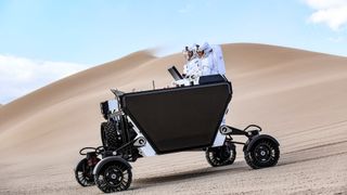 two people in space suits drive a lunar rover through the california desert