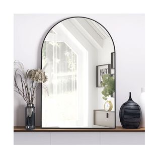 black framed arch wall mirror on shelf with vases left and right