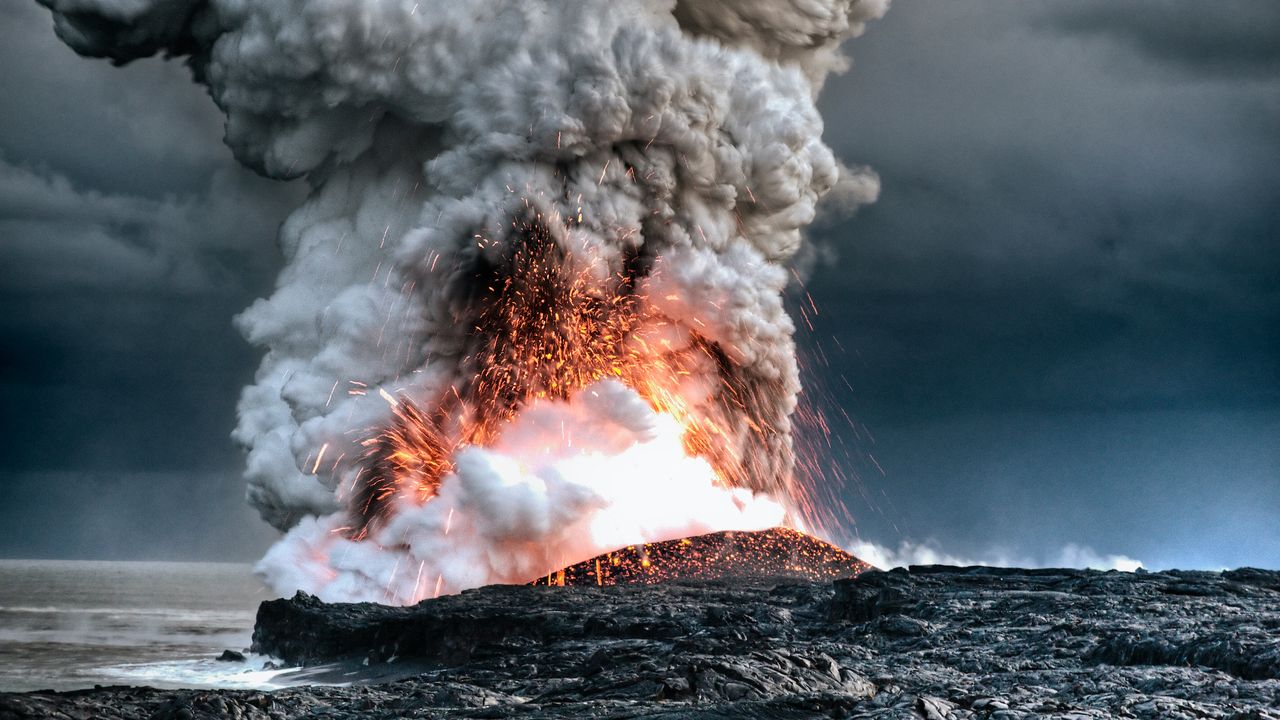 A volcano erupts in Hawaii near the water.