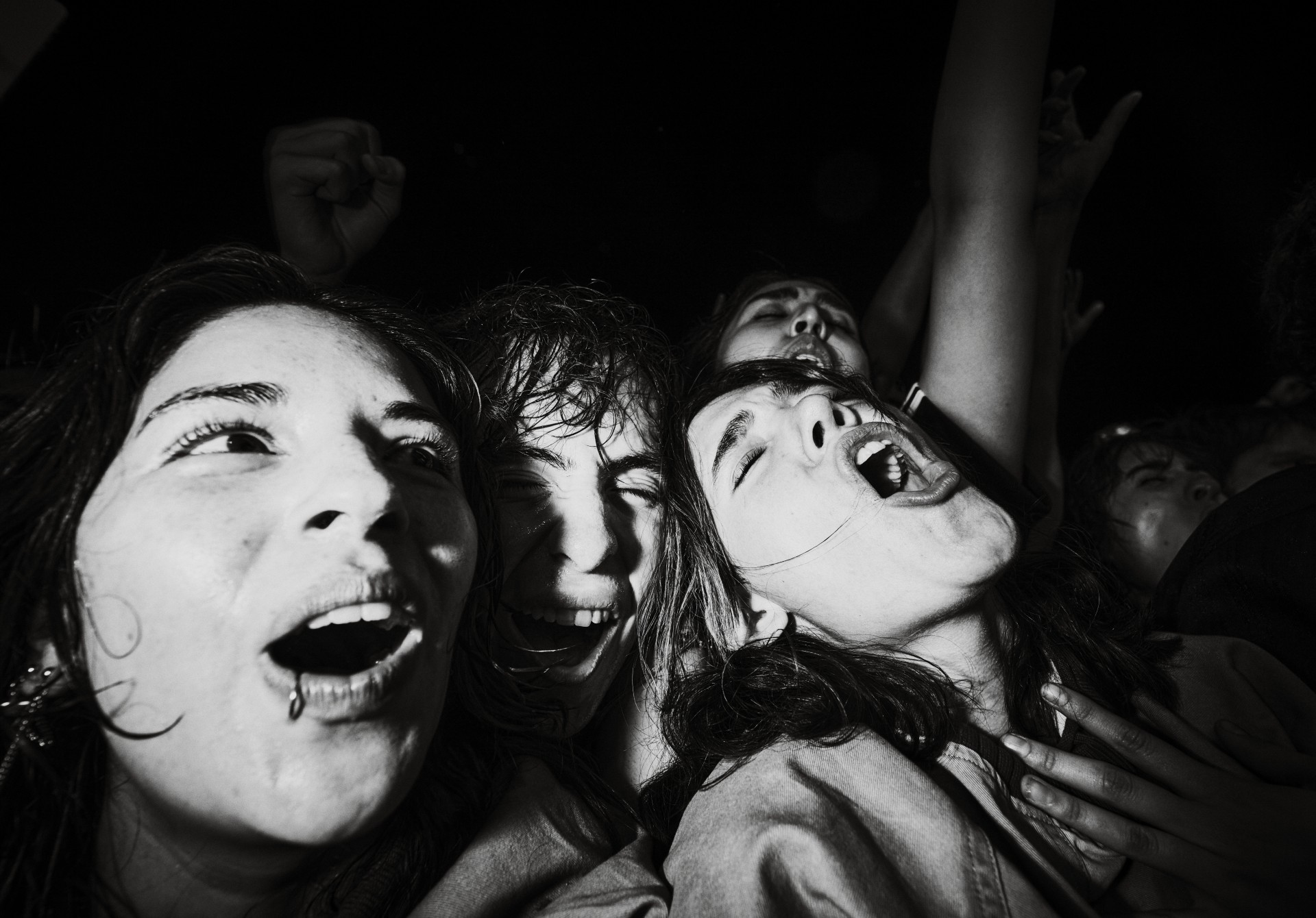 An intense, close-up black-and-white photo captures the raw emotion and excitement of several fans screaming in the front row of a concert.