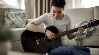 Women sits down playing a black acoustic guitar