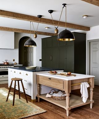 White kitchen island with wooden island next to it, beams and pendant lighting hanging from ceiling