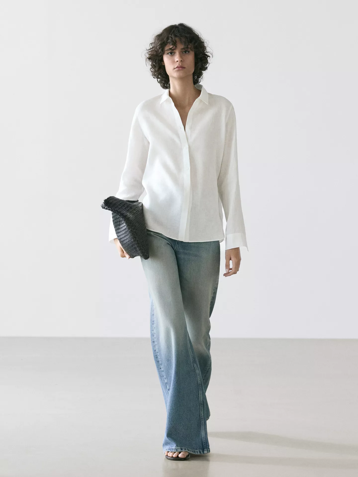 A model wearing a white Massimo Dutti linen shirt with jeans and a black bag.