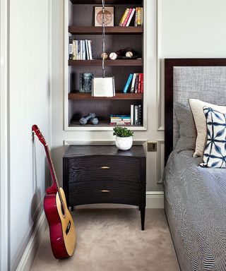 Bedroom, grey headboard and bedding, alcove shelves decorated with books and ornaments, guitar on floor