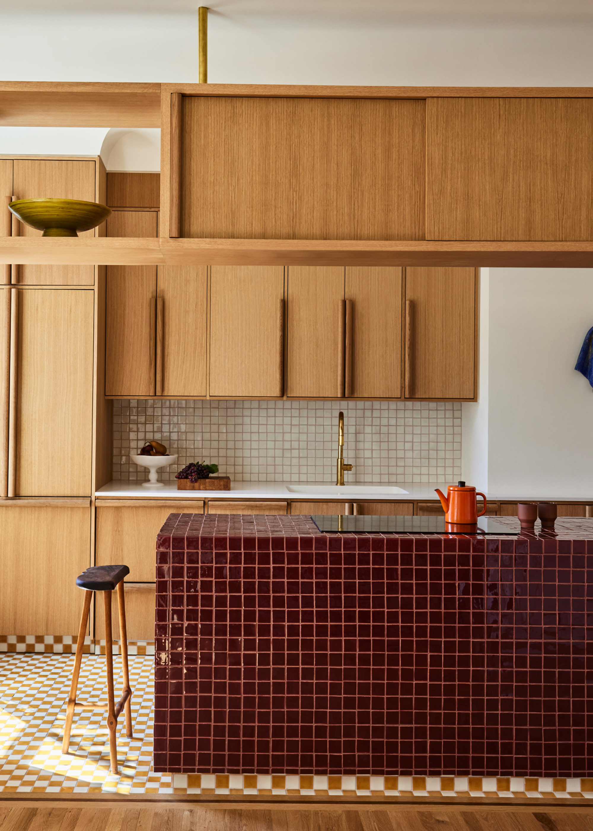 a kitchen with a tiled island and wooden oak kitchen cabinets opposite it with open and closed shelving