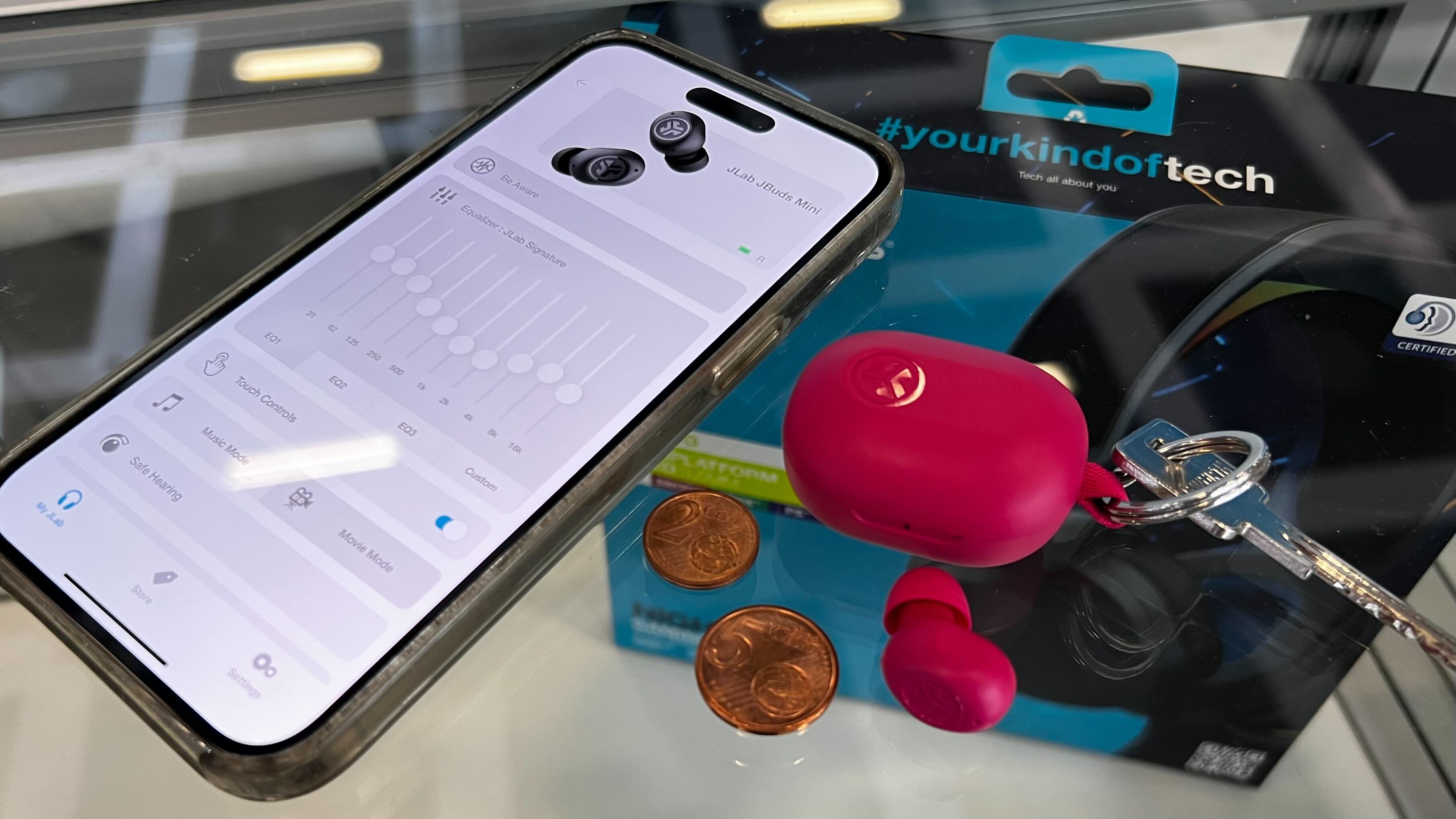 The JLab JBuds Mini earbuds on a keyring next to a phone