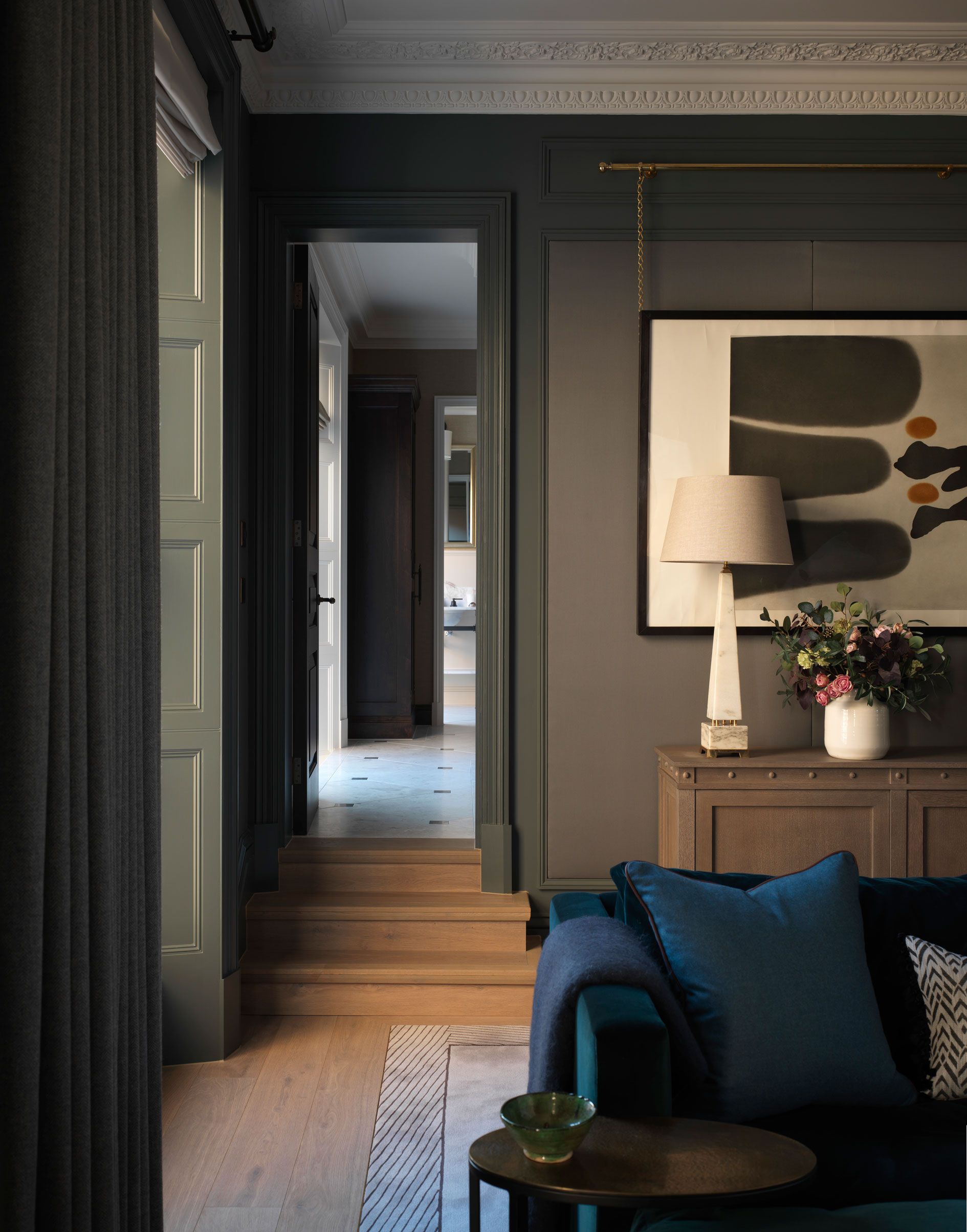 dark painted living room with light coloured modern painting, lamp and vase, blue sofa and cushions, wooden floor