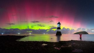 Vibrant green and red pillars of light in the sky above a lighthouse. 