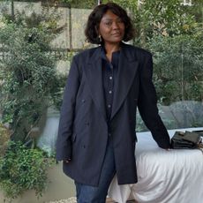 Franny Mozemba is photographed wearing a navy pinstripe blazer and navy button-up top with dark jeans.
