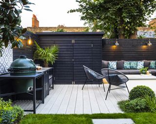 A contemporary outdoor seating area with white pavers and a black fence and built in w ooden garden sotrage