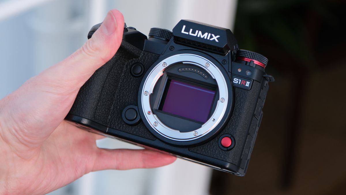 Panasonic Lumix S1R II camera held in a hand outside with no lens attached and the sensor showing