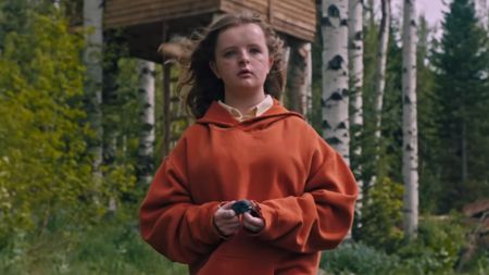 Milly Shapiro as Charlie in Hereditary wearing an orange sweater and holding a pigeon head