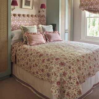 A bed in the centre of a room, with contrasting patterned throws and cushions, and a white valance underneath