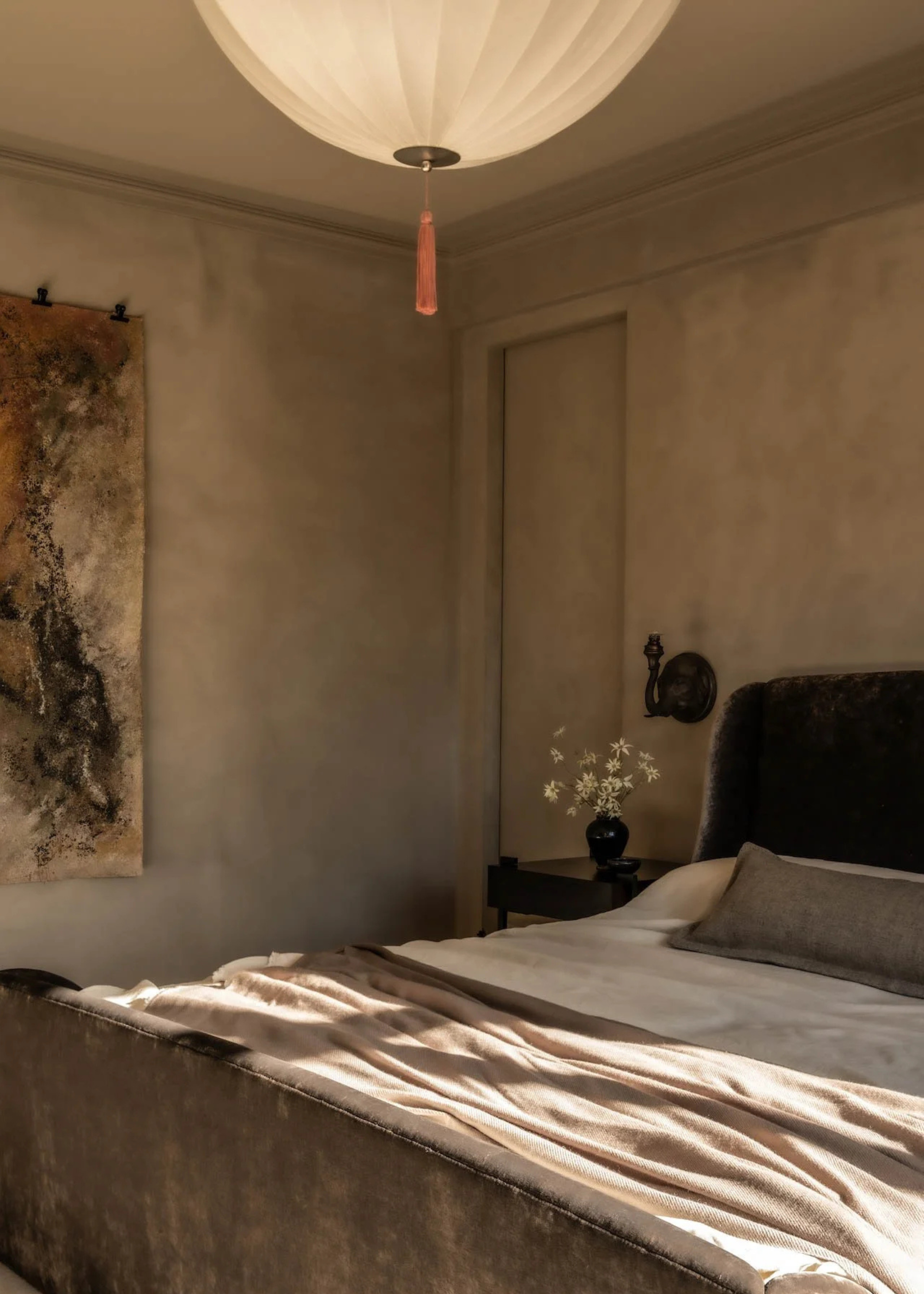 A rustic limewash bedroom with a pendant paper lamp and a hanging tapestry