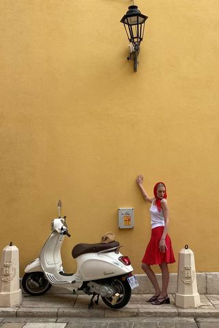 a photo showing what colors go with red, specifically a woman wearing a red skirt with a white tank top and red scarf and black sandals