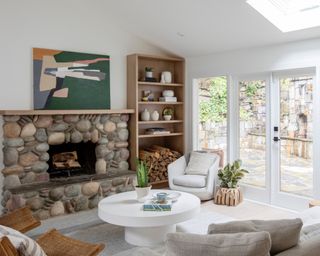 living room furniture arranging mistakes, large focal fireplace with stones, bookcase, artwork, view outside, circular white coffee table, chairs and couches, artwork