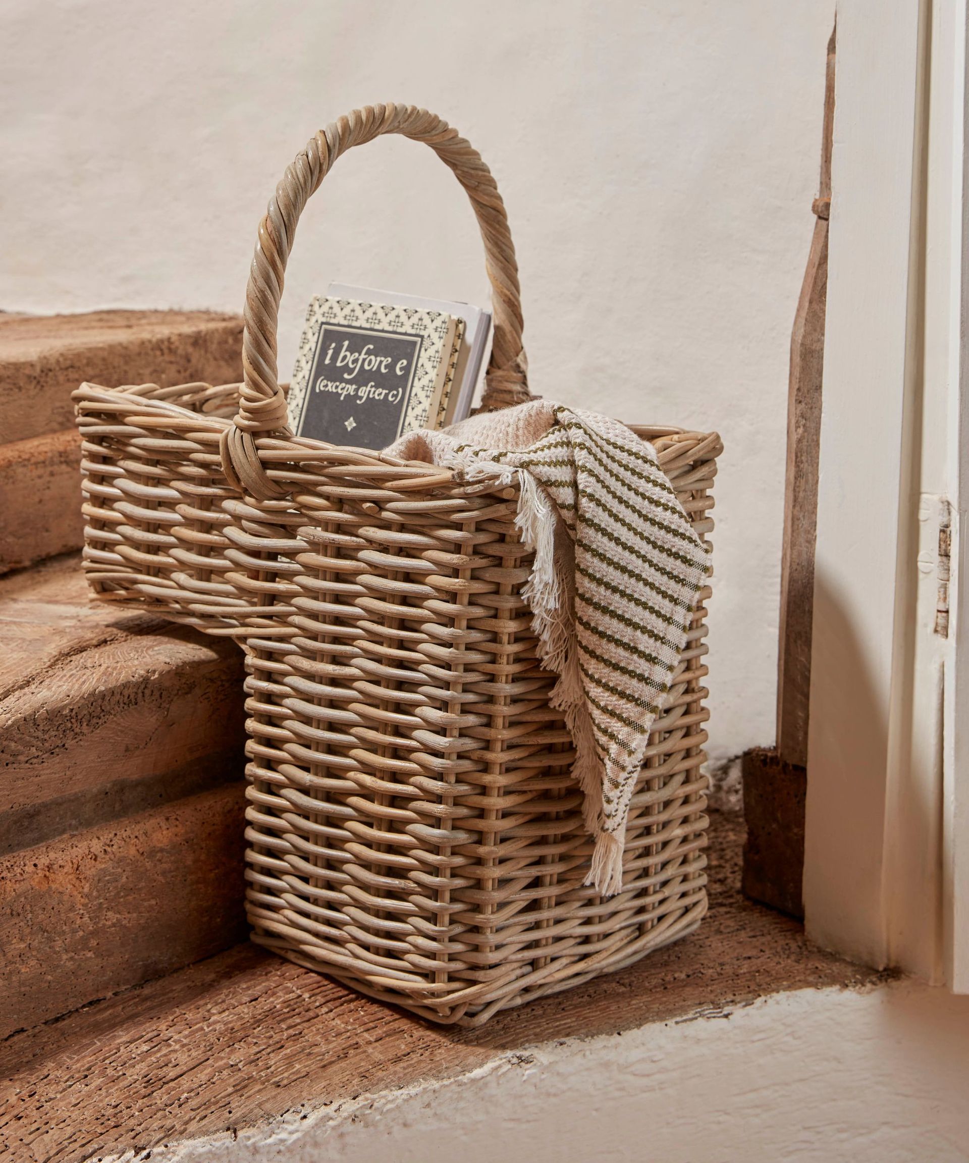 A woven wicker stairs basket with an arched handle. On the edge of a stone step.