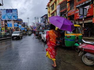 A woman holds an umbrella while walking on the street during rain due to Cyclone Dana in Kolkata, India