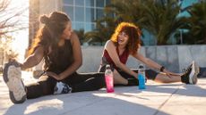 two women sit on the ground stretching their legs