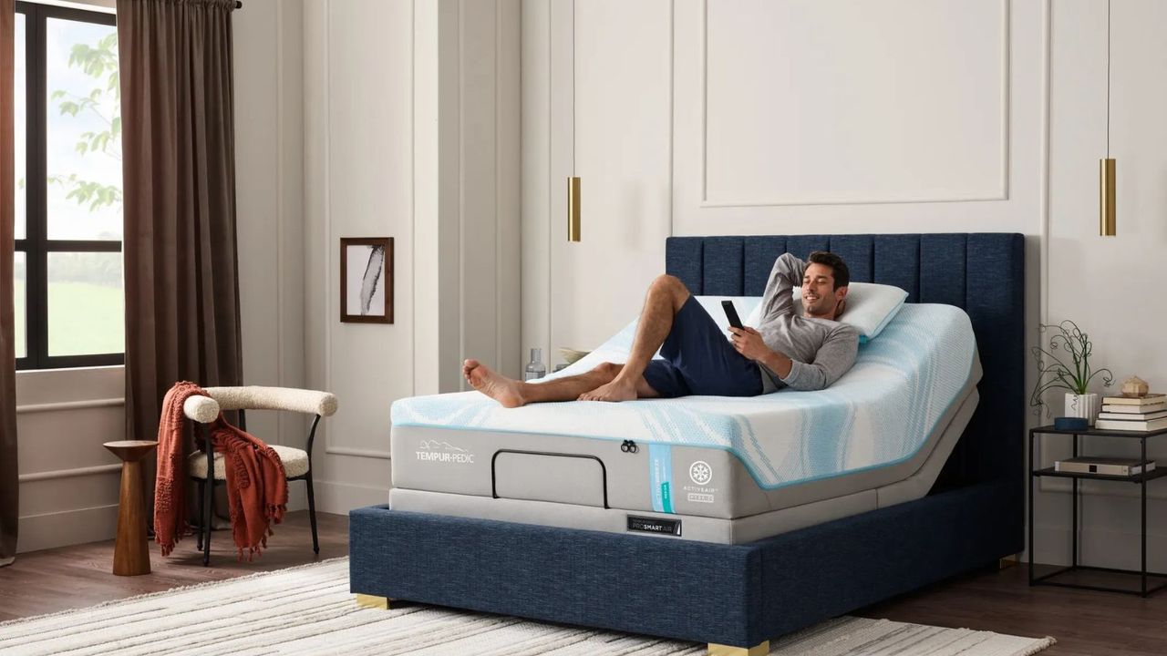 A man lying on a Tempur-Pedic mattress on a blue bed frame against a white wall.