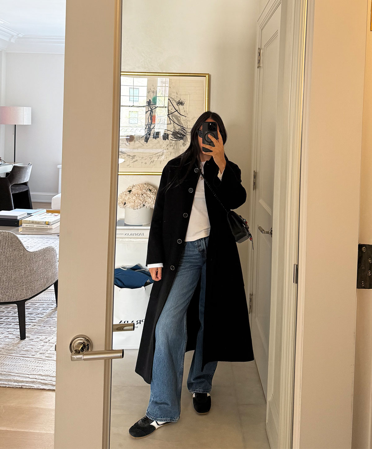 @nicoleakhtarzad taking a mirror outfit selfie and wearing a coat, jeans, and sneakers.