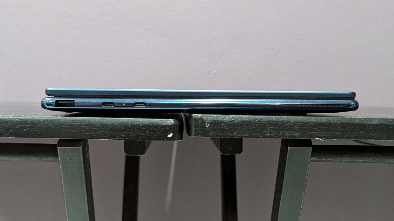 A straight-on view of the side of a laptop, showing its connectivity ports, on top of a black table