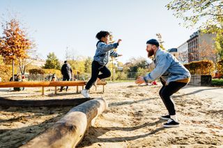 child jumping off log at park and into his parent's arms