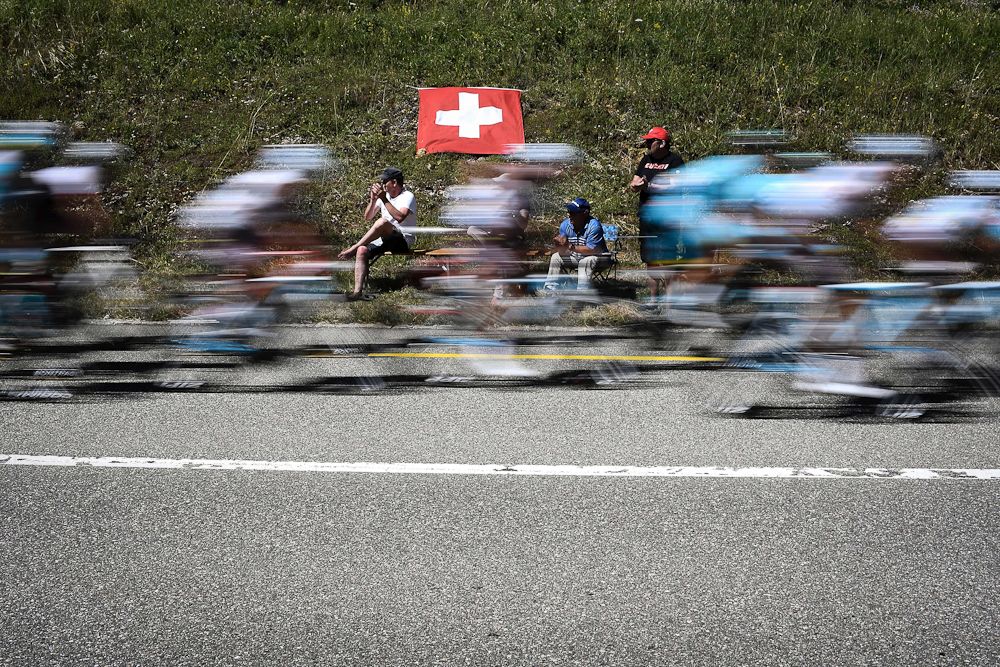 A breeze fills out the Swiss flag as the peloton flies by during stage 16