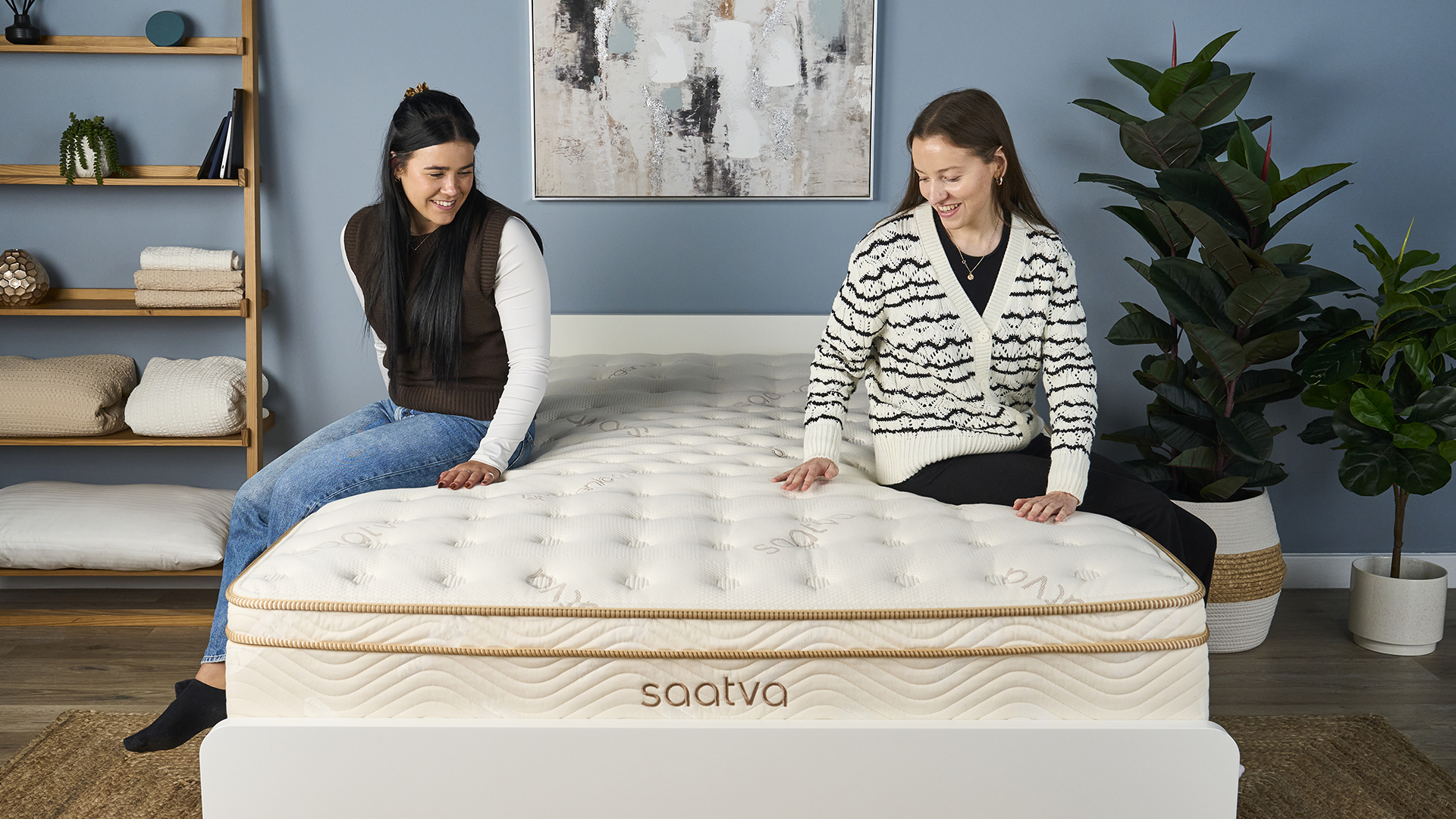 Two mattress testers sit on the Saatva Classic mattress on a bed frame in the TOm's Guide sleep studio