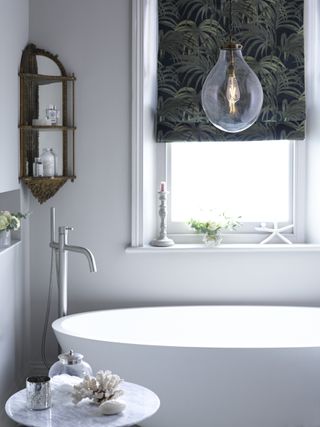 A white bathroom with a curved bath and a large overhanging pendant filament light bulb