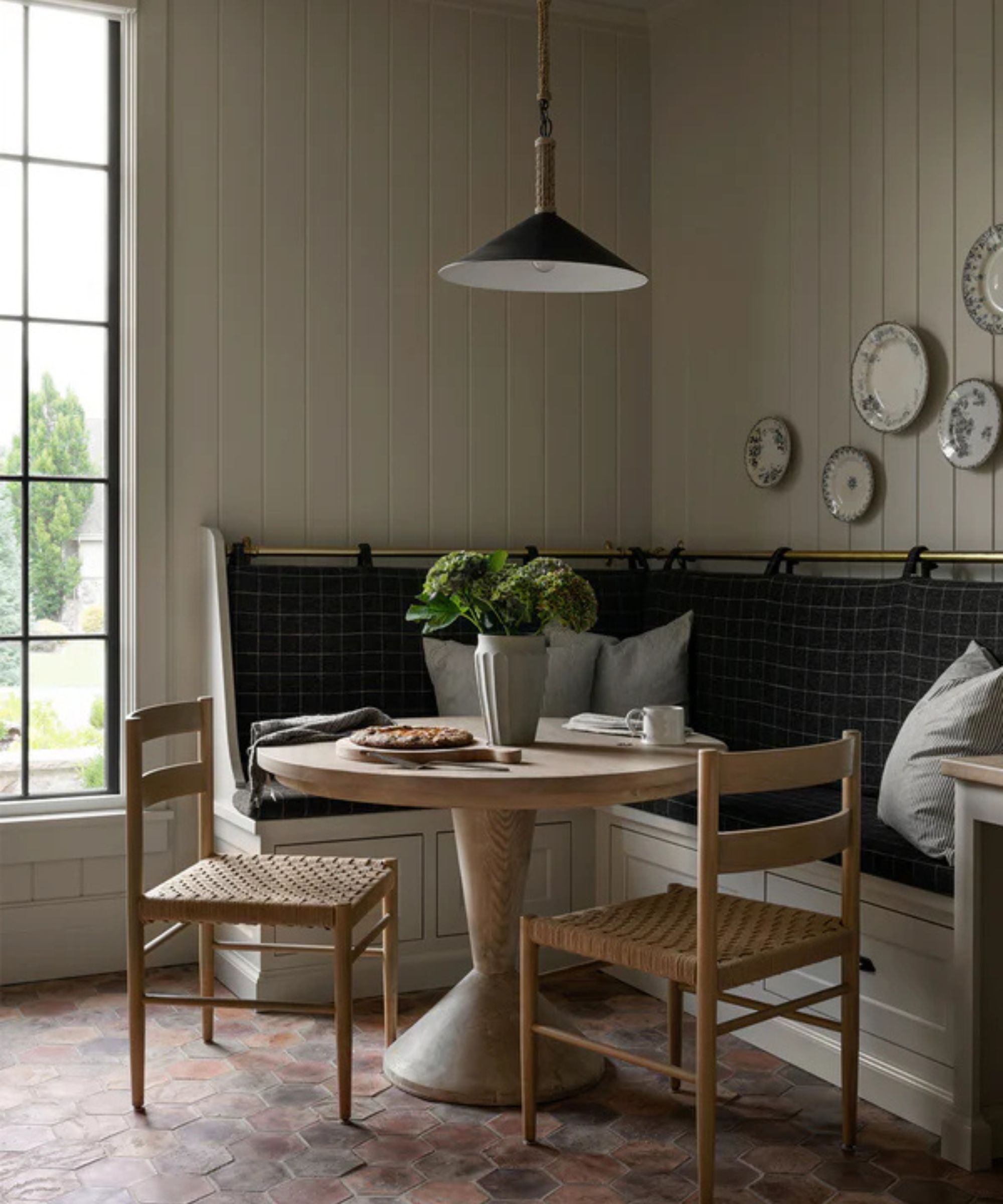 A warm neutral kitchen corner with a L-shaped banquette, round pedestal table, and two woven chairs
