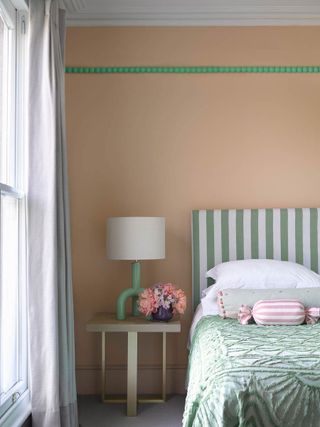 Small bedroom painted in springtime peach, accented with green trim that brings out pinstripe headboard
