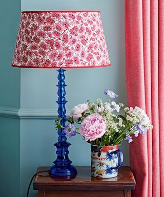 Floral fabric lampshade on blue base next to mug of flowers