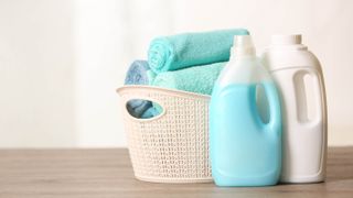 Two bottles of laundry detergent in front of a hamper filled with towels