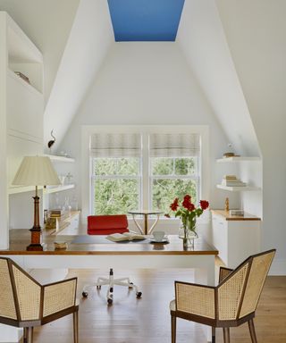 Home office with white walls with desk and office chair and two visitor chairs opposite, storage furniture, wood floor and high ceiling painted in blue