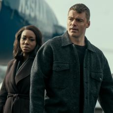 Amanda Warren as Catherine Weaver, Gabriel Basso as Peter Sutherland wearing coats and standing outside of a plane on a jetway in the night agent season 3