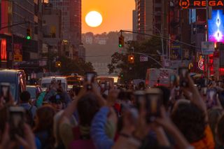 eople stand on 42nd Street in Times Square as they photograph the second evening of the Manhattanhenge sunset on May 30, 2023, in New York City.