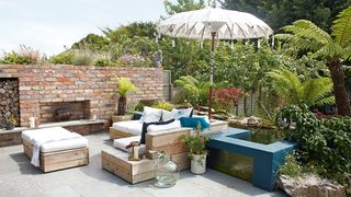 An outdoor seating area with a built in brick outdoor fire and jungle style planitng