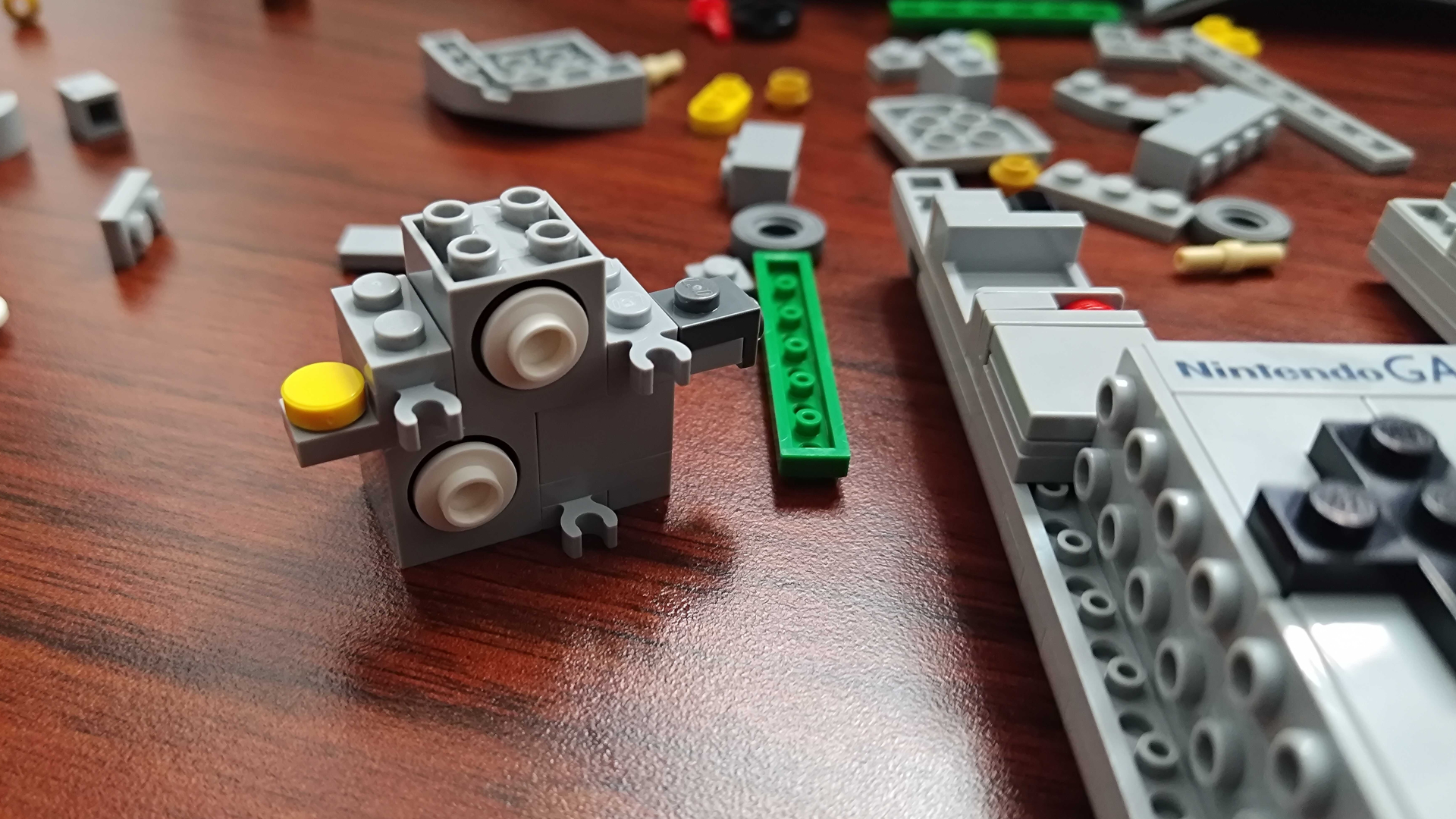 A series of part-built pieces for the Lego Game Boy, laid out on a wooden table